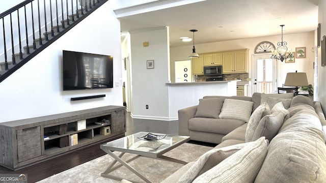 living room featuring baseboards, a notable chandelier, dark wood finished floors, and stairs