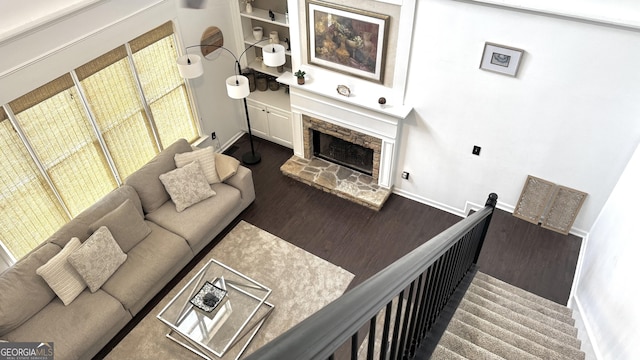 living room with baseboards, a stone fireplace, and wood finished floors