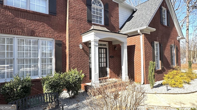 entrance to property with brick siding and a shingled roof