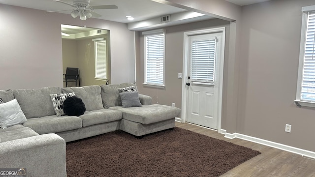 living room featuring a ceiling fan, visible vents, wood finished floors, and baseboards