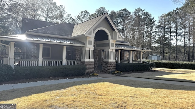 view of front of property with brick siding, a porch, a front lawn, and a standing seam roof