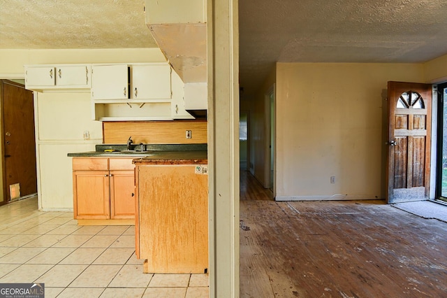 kitchen featuring a sink, dark countertops, a textured ceiling, light wood finished floors, and baseboards