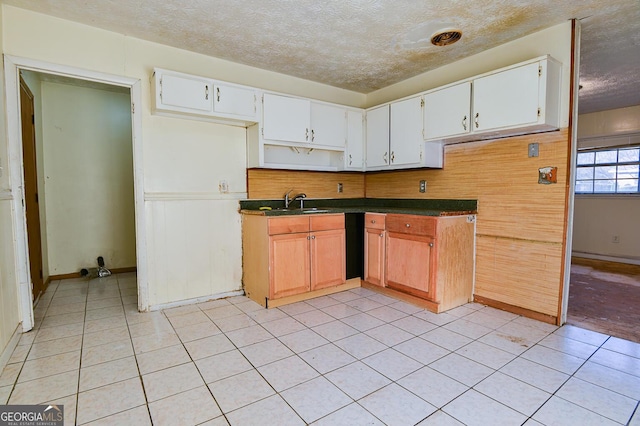 kitchen with a sink, a textured ceiling, dark countertops, white cabinetry, and light tile patterned floors