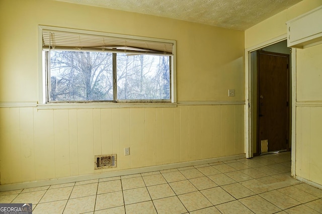 empty room featuring light tile patterned flooring, visible vents, wainscoting, and a textured ceiling