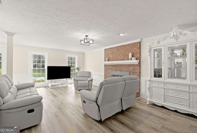 living room with a wainscoted wall, ornamental molding, a textured ceiling, wood finished floors, and a brick fireplace