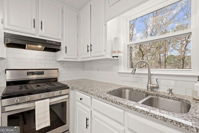 kitchen featuring tasteful backsplash, under cabinet range hood, gas stove, white cabinetry, and a sink