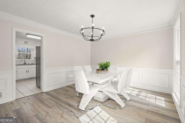 unfurnished dining area with a wainscoted wall, an inviting chandelier, light wood-style flooring, a sink, and crown molding