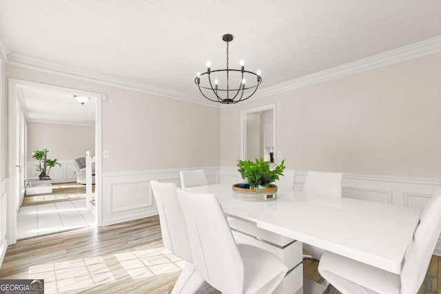 dining room featuring a chandelier, a wainscoted wall, ornamental molding, light wood-style flooring, and a decorative wall