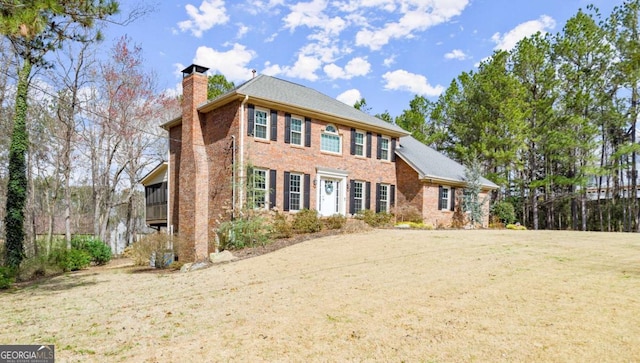 colonial home featuring brick siding, a chimney, and a front lawn