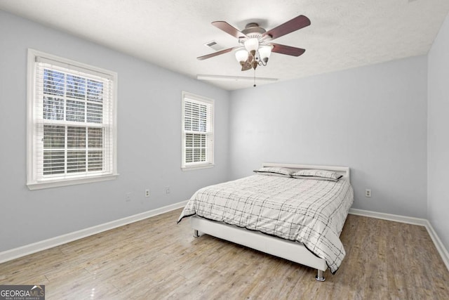 bedroom with visible vents, ceiling fan, baseboards, and wood finished floors