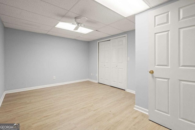 unfurnished bedroom with baseboards, ceiling fan, a paneled ceiling, a closet, and light wood-type flooring