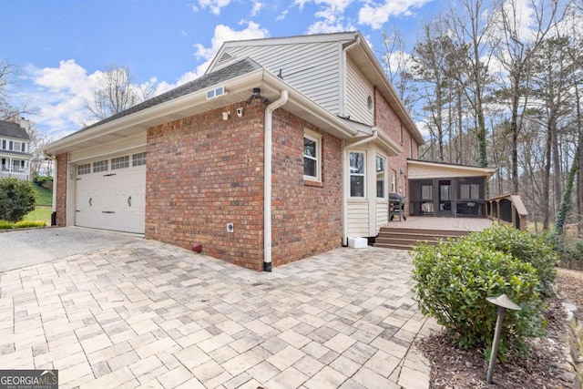 view of home's exterior with decorative driveway, an attached garage, brick siding, and a sunroom