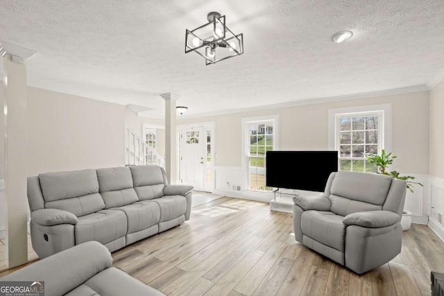 living area featuring light wood-type flooring, a textured ceiling, ornamental molding, and wainscoting