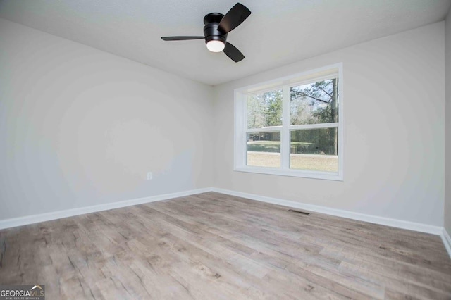 empty room with ceiling fan, wood finished floors, visible vents, and baseboards