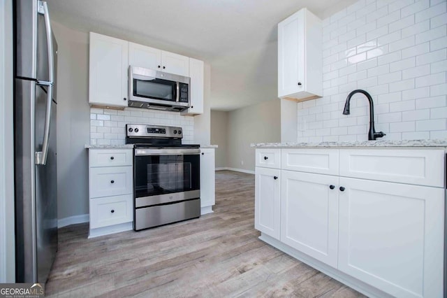 kitchen featuring light wood-style flooring, backsplash, white cabinets, and appliances with stainless steel finishes