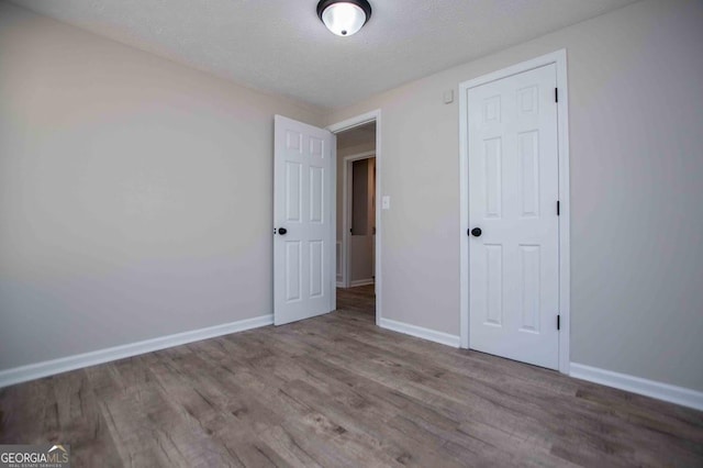 unfurnished bedroom featuring wood finished floors, baseboards, and a textured ceiling