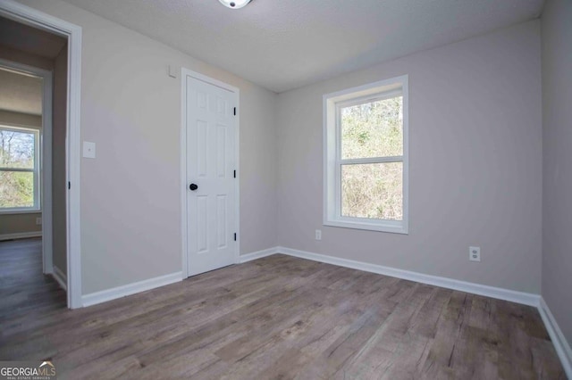 unfurnished bedroom with multiple windows, wood finished floors, baseboards, and a closet