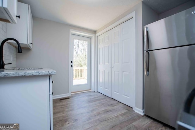 kitchen featuring light stone counters, visible vents, freestanding refrigerator, light wood-style floors, and white cabinetry