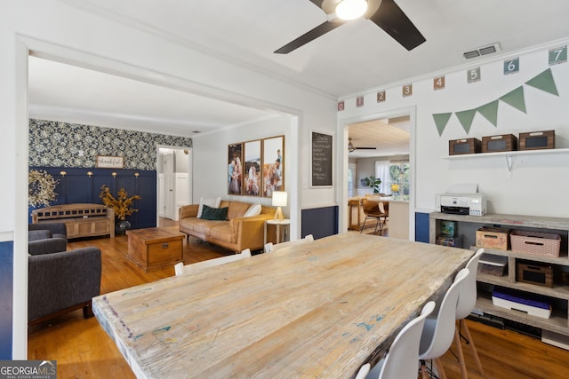 dining room featuring visible vents, wallpapered walls, crown molding, ceiling fan, and wood finished floors