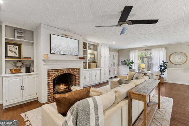 living room featuring built in shelves, a ceiling fan, dark wood-style floors, a fireplace, and baseboards