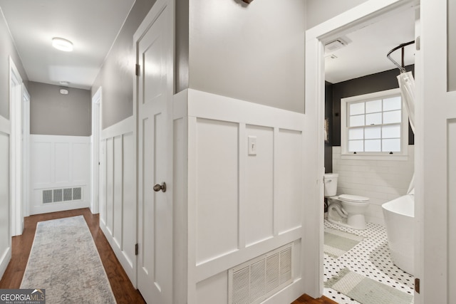 corridor featuring visible vents, wainscoting, and dark tile patterned flooring