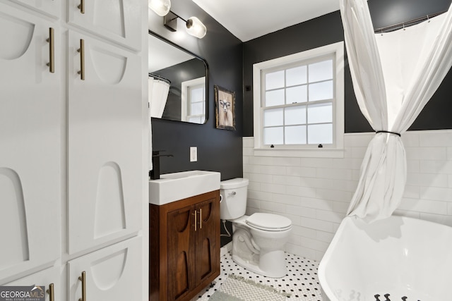 full bathroom with toilet, tile walls, wainscoting, tile patterned flooring, and vanity