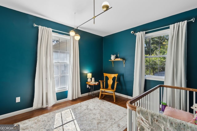 bedroom with baseboards, a nursery area, and wood finished floors