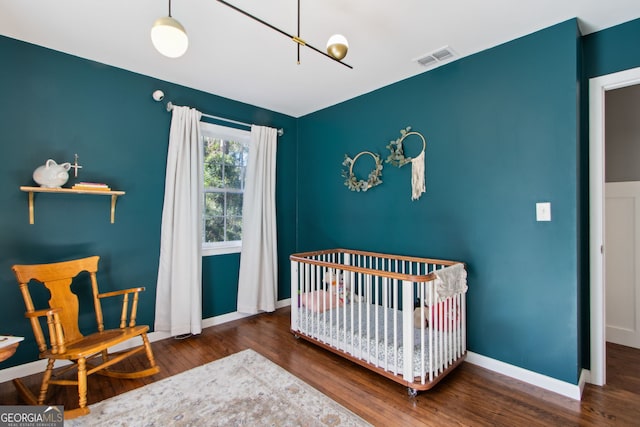 bedroom with a crib, wood finished floors, visible vents, and baseboards