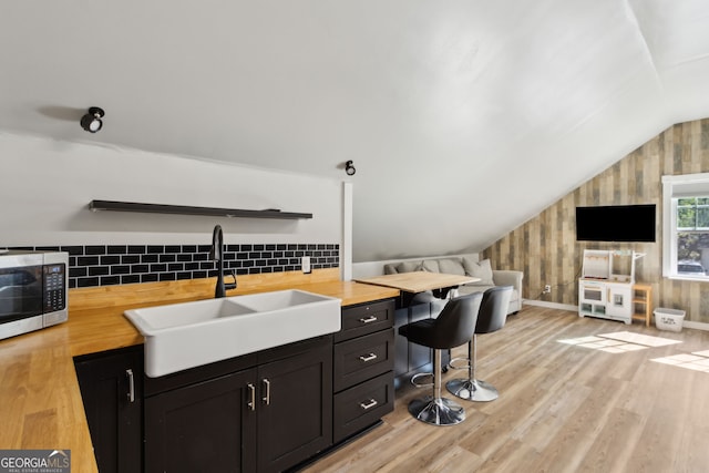 office featuring a sink, baseboards, light wood-style floors, and vaulted ceiling