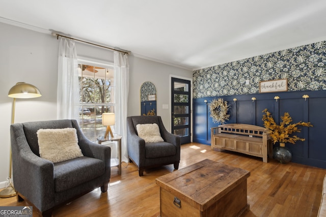 living area featuring wallpapered walls, an accent wall, light wood-type flooring, and ornamental molding