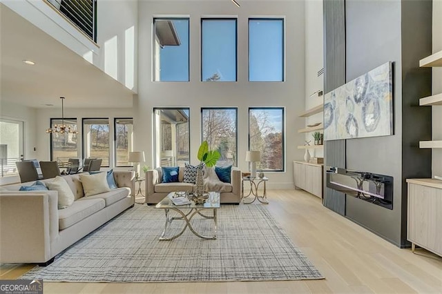 living area with a notable chandelier, plenty of natural light, baseboards, and light wood-type flooring