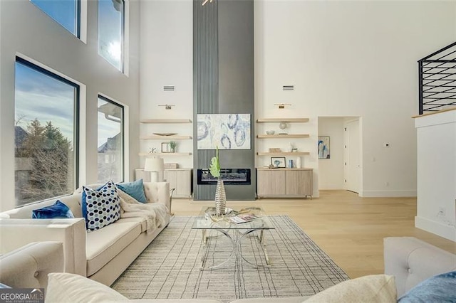 living room with light wood-type flooring, baseboards, and a high ceiling