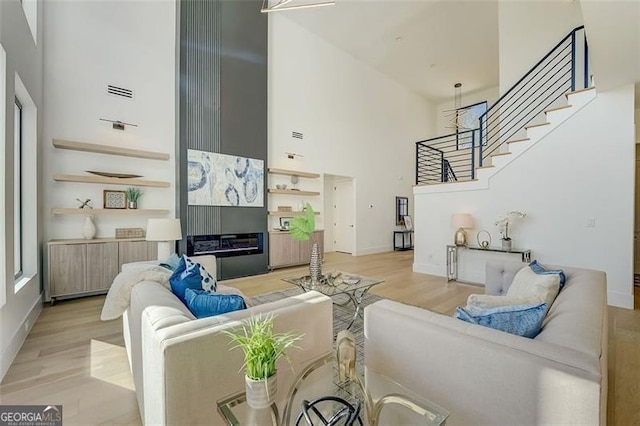 living room featuring light wood-type flooring, a towering ceiling, stairs, and radiator heating unit