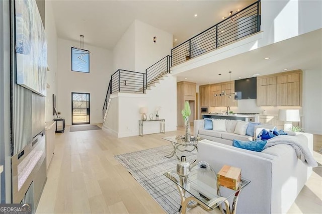 living area featuring stairway, baseboards, light wood-style floors, and a towering ceiling