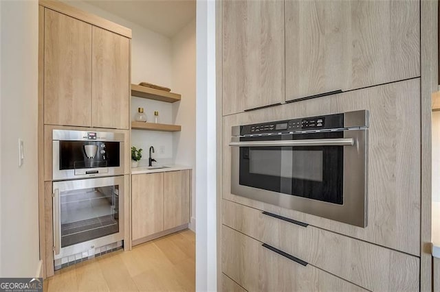 kitchen featuring a sink, open shelves, stainless steel double oven, and light brown cabinetry