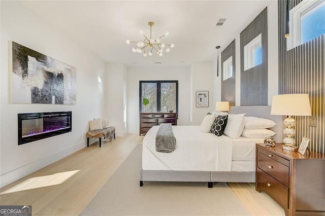 bedroom with a glass covered fireplace, visible vents, a notable chandelier, and wood finished floors