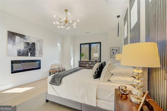 bedroom with a notable chandelier, a glass covered fireplace, and wood finished floors