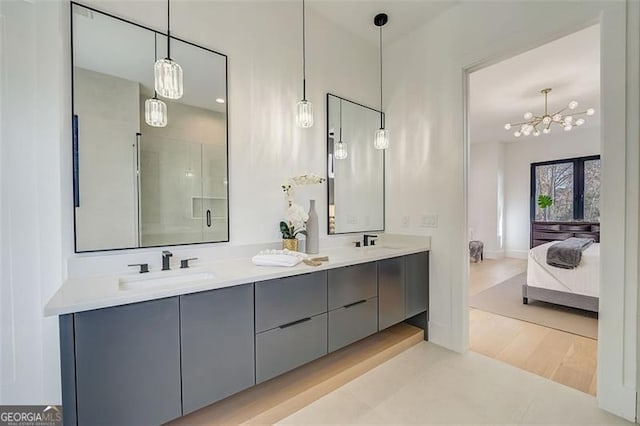 ensuite bathroom with double vanity, a shower stall, an inviting chandelier, and a sink