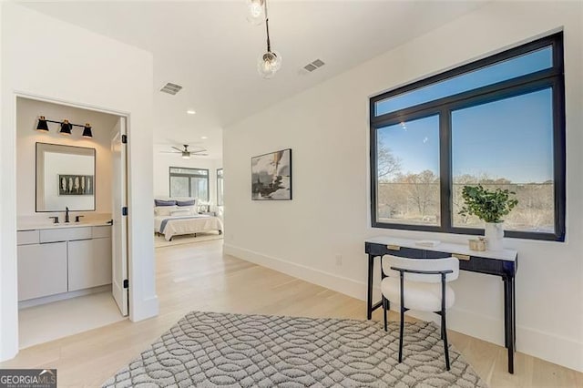 hall with visible vents, light wood-type flooring, baseboards, and a sink