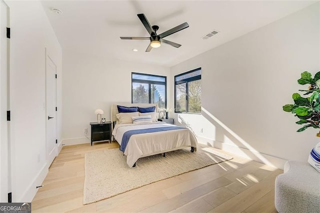 bedroom featuring ceiling fan, visible vents, baseboards, and light wood-style flooring