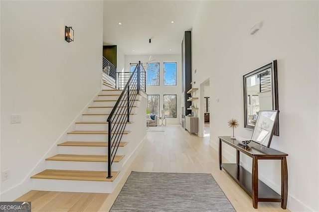 stairs with baseboards, wood finished floors, and a towering ceiling