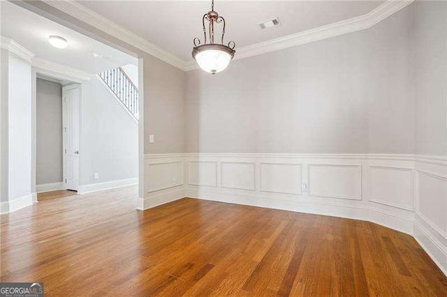 unfurnished room featuring wood finished floors, visible vents, and ornamental molding