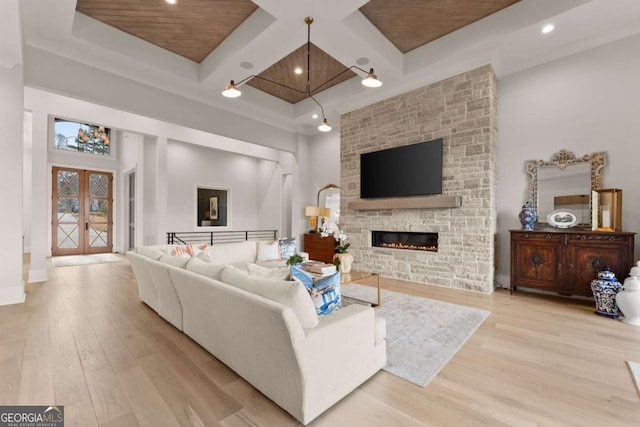 living room with beam ceiling, coffered ceiling, wood finished floors, french doors, and a large fireplace