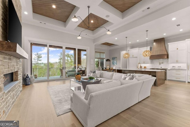 living room with plenty of natural light, light wood-style flooring, coffered ceiling, and a stone fireplace