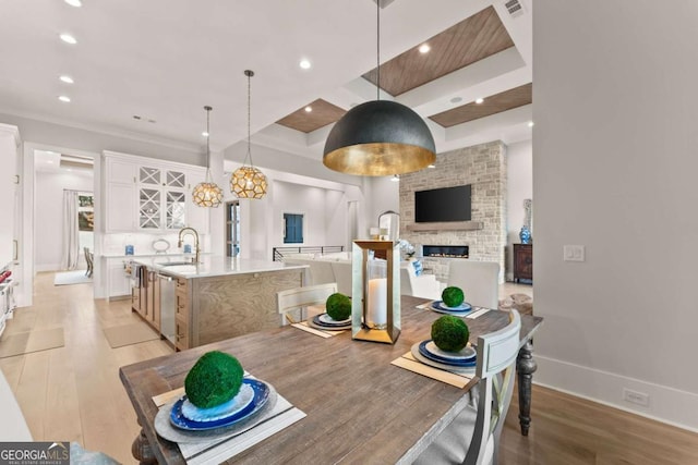 dining area with a tray ceiling, recessed lighting, a fireplace, light wood finished floors, and baseboards
