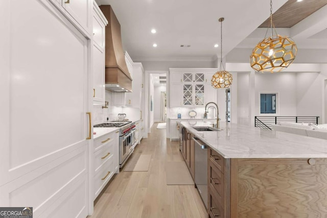 kitchen with light wood-type flooring, a sink, backsplash, appliances with stainless steel finishes, and custom exhaust hood