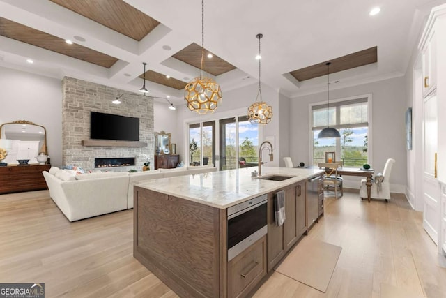 kitchen featuring coffered ceiling, plenty of natural light, a fireplace, a sink, and light wood-type flooring