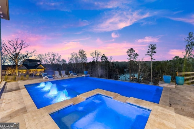 pool at dusk featuring a patio area, a pool with connected hot tub, and fence