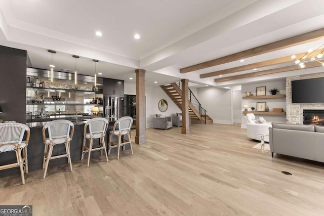 interior space with light wood finished floors, dark countertops, open floor plan, a stone fireplace, and a kitchen breakfast bar