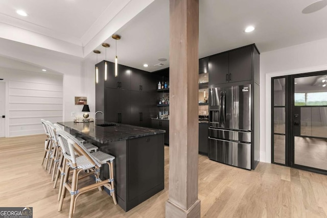 kitchen with dark cabinetry, a sink, light wood-style floors, a kitchen bar, and refrigerator with ice dispenser